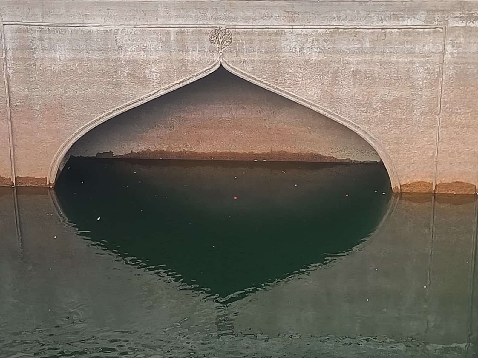 Beautiful archway reflected in tranquil water, reminiscent of the serene ambiance found near grand mausoleums. Perfect spot for Manganiyars' melodies.